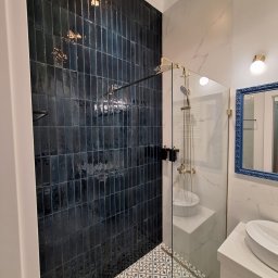 Paweł Albert Twój Kwadrat - Elegancka łazienka po remoncie: ciemne, pionowe płytki na ścianie kabiny prysznicowej, wzorzysta podłoga i marmurowe wykończenia. Złote detale armatury.