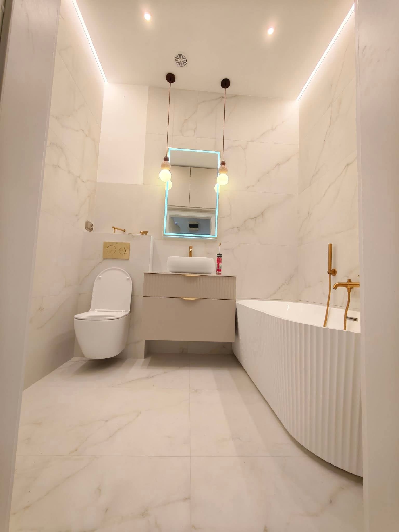 Elegancka łazienka w bieli i beżu: marmurowe płytki, podświetlane lustro, designerska wanna z żłobieniami i złota armatura. Nowoczesny minimalizm.