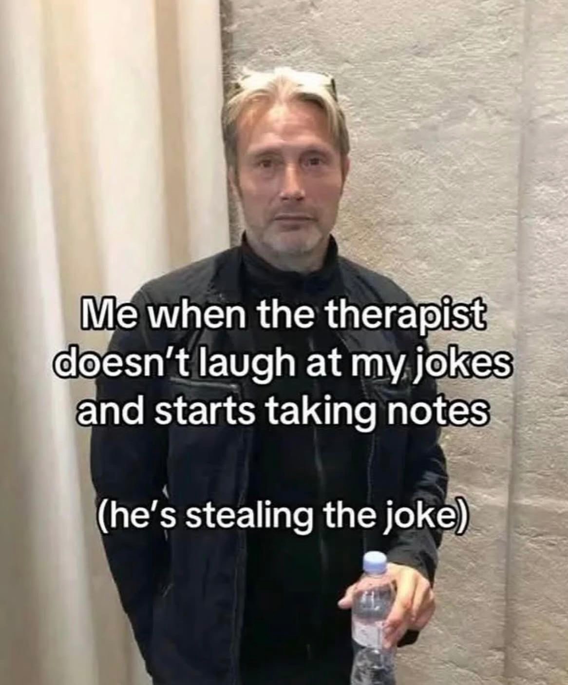 Mężczyzna z butelką wody, z wyrazem twarzy sugerującym brak rozbawienia, w kontekście żartu niezrozumianego przez terapeutę, który robi notatki.