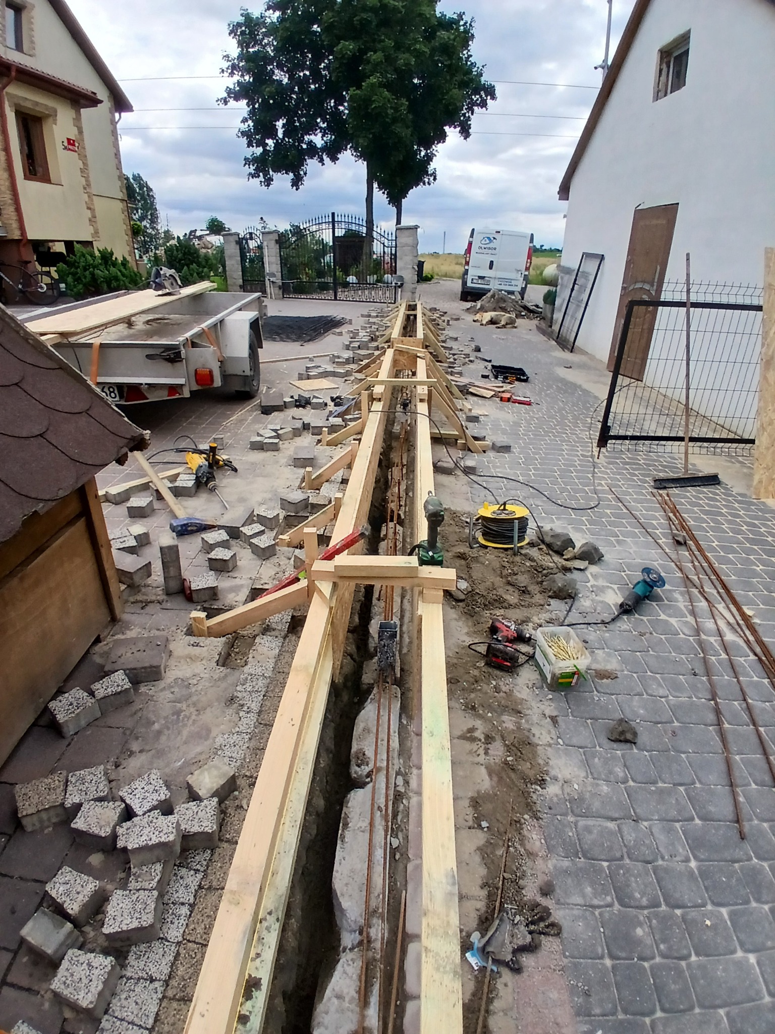 Przygotowanie podłoża pod nawierzchnię z kostki brukowej: wykop, szalunek z desek, narzędzia budowlane. Widok z góry na plac budowy przed domem.