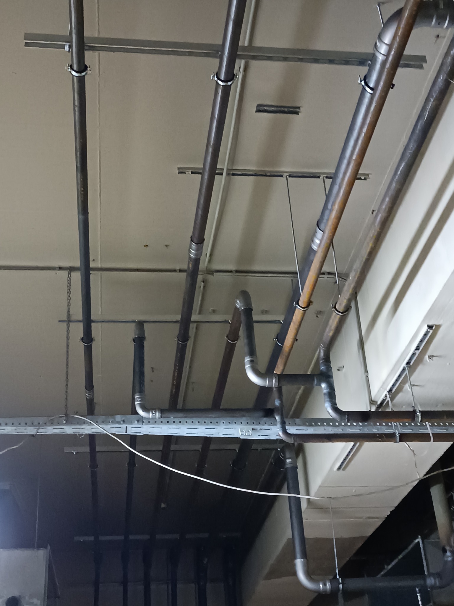 Skomplikowany układ rur instalacji pod stropem, widoczne różne materiały i łączenia, wsporniki mocujące.