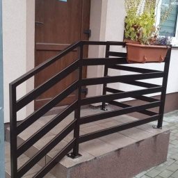 USŁUGI SPAWALNICZE KRYSTIAN PAWŁOWSKI - Nowoczesna, brązowa balustrada schodowa z poziomymi szczeblami, z donicą z kwiatami, przy wejściu do budynku z brązowymi drzwiami i oknem.