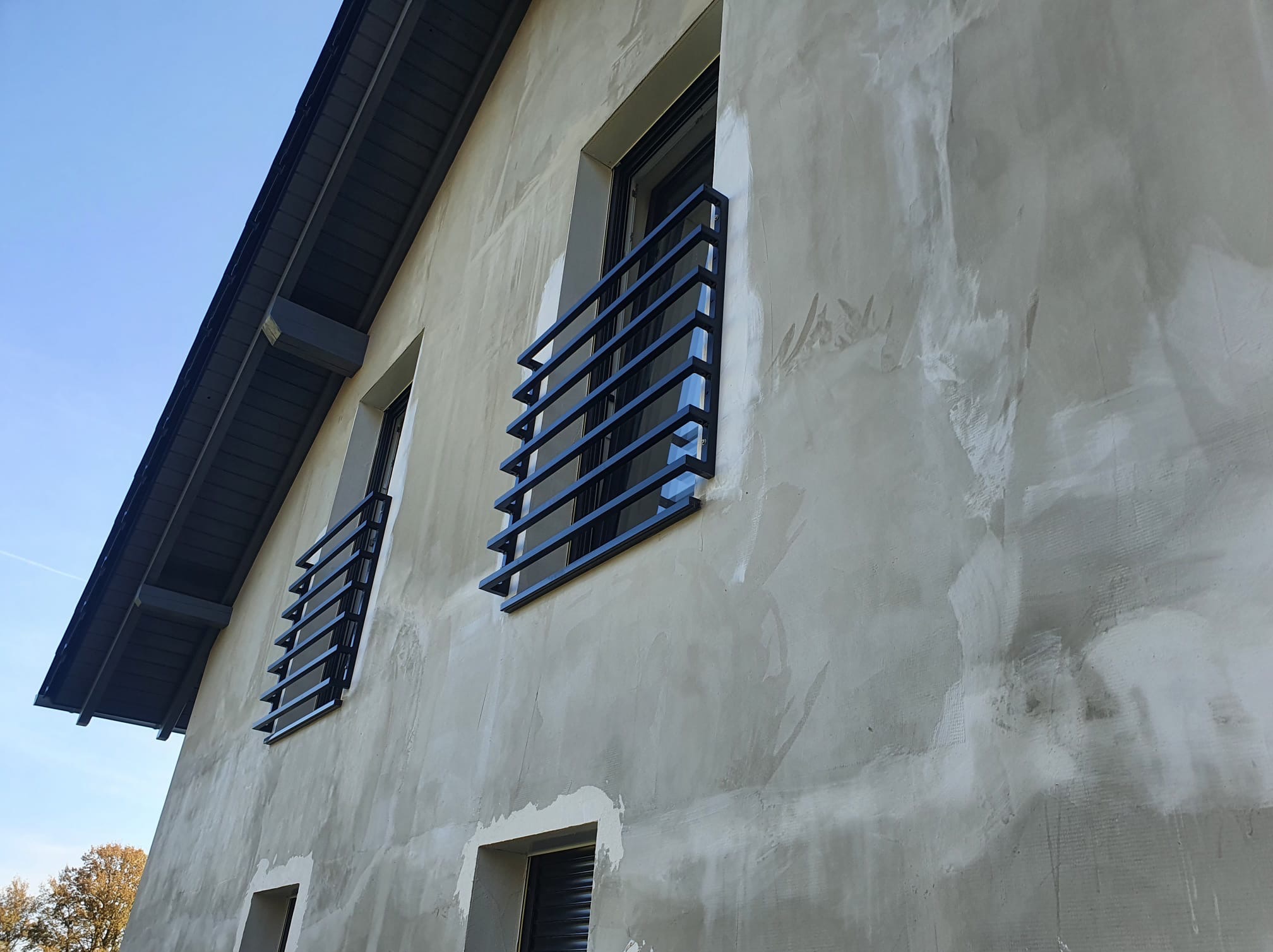 Elewacja domu z zamontowanymi, nowoczesnymi, czarnymi balustradami okiennymi. Widok z dołu, podkreślający geometrię i surowy styl.