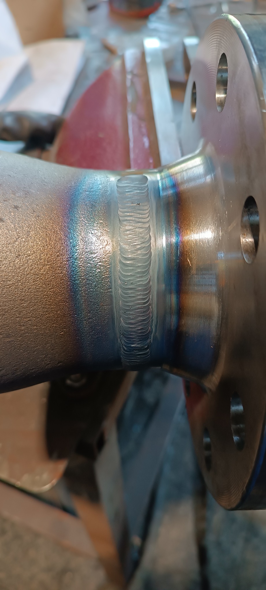 Precyzyjne spawy na metalowym elemencie z widocznymi tęczowymi przebarwieniami termicznymi, ukazujące umiejętności spawacza w zbliżeniu.