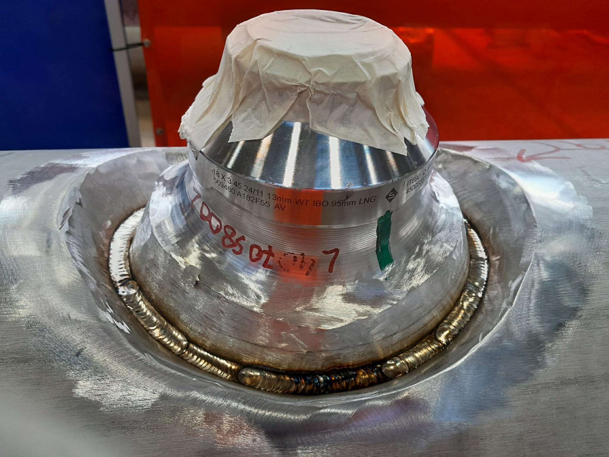 Precyzyjne spawanie kołnierza rury ze stali nierdzewnej, zabezpieczonego papierem, z widocznymi śladami obróbki i oznaczeniami technicznymi. Detal spawalniczy.