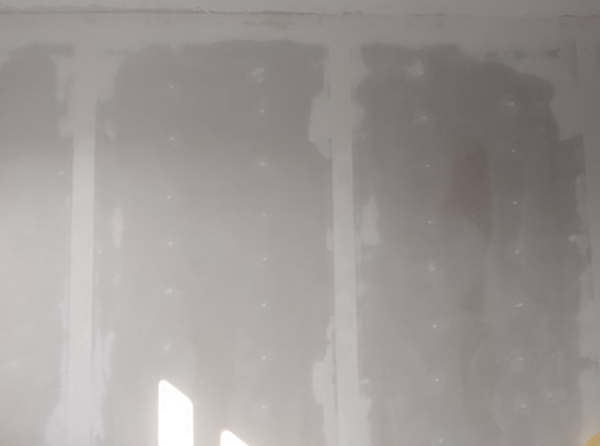 Ściana po nałożeniu gładzi szpachlowej, widoczne łączenia płyt gipsowych wzmocnione taśmą. Przygotowanie do dalszych prac wykończeniowych.