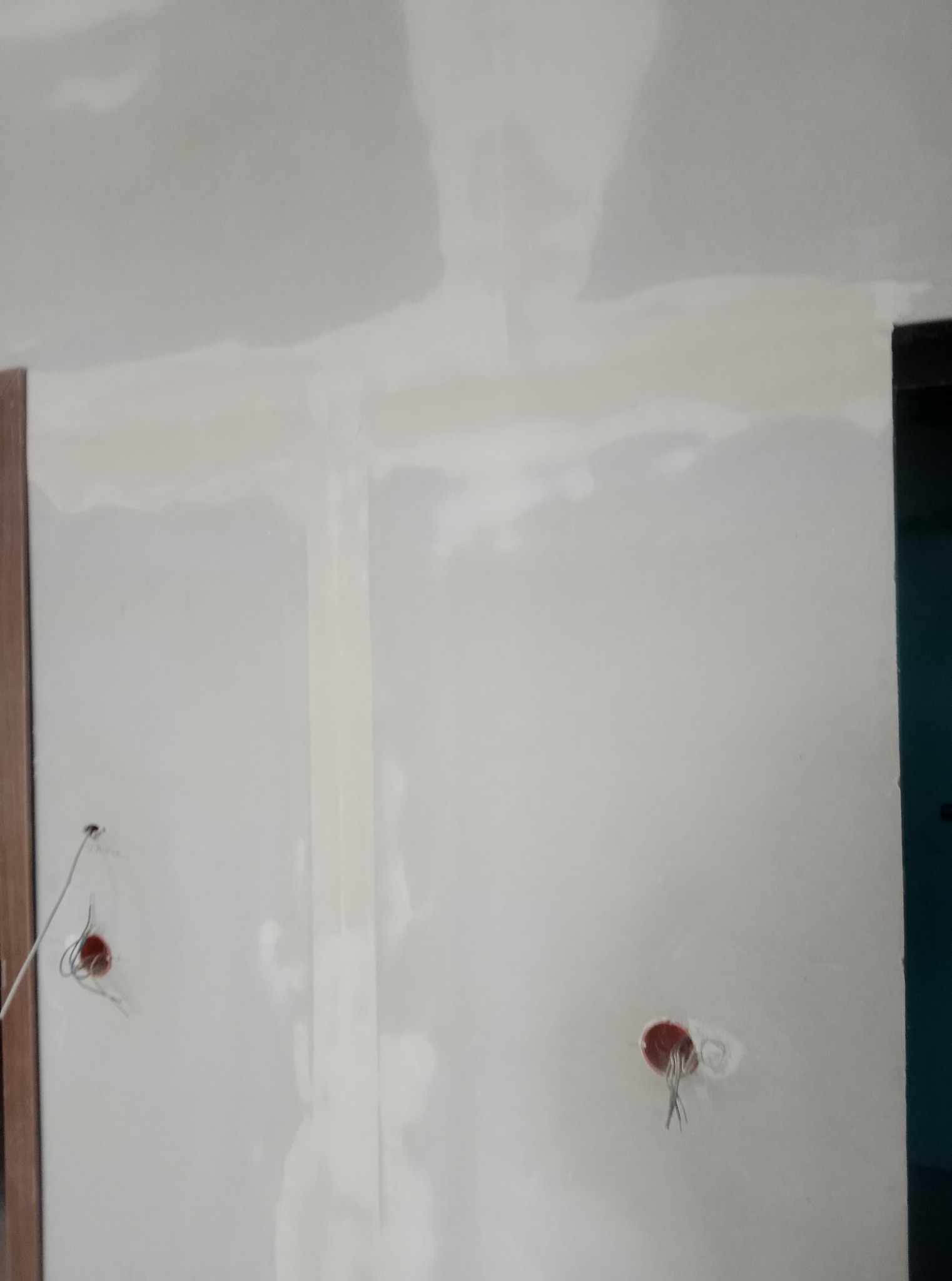 Ściana po nałożeniu gładzi, widoczne puszki elektryczne. Przygotowanie do malowania. Fragment ościeżnicy po lewej stronie kadru.