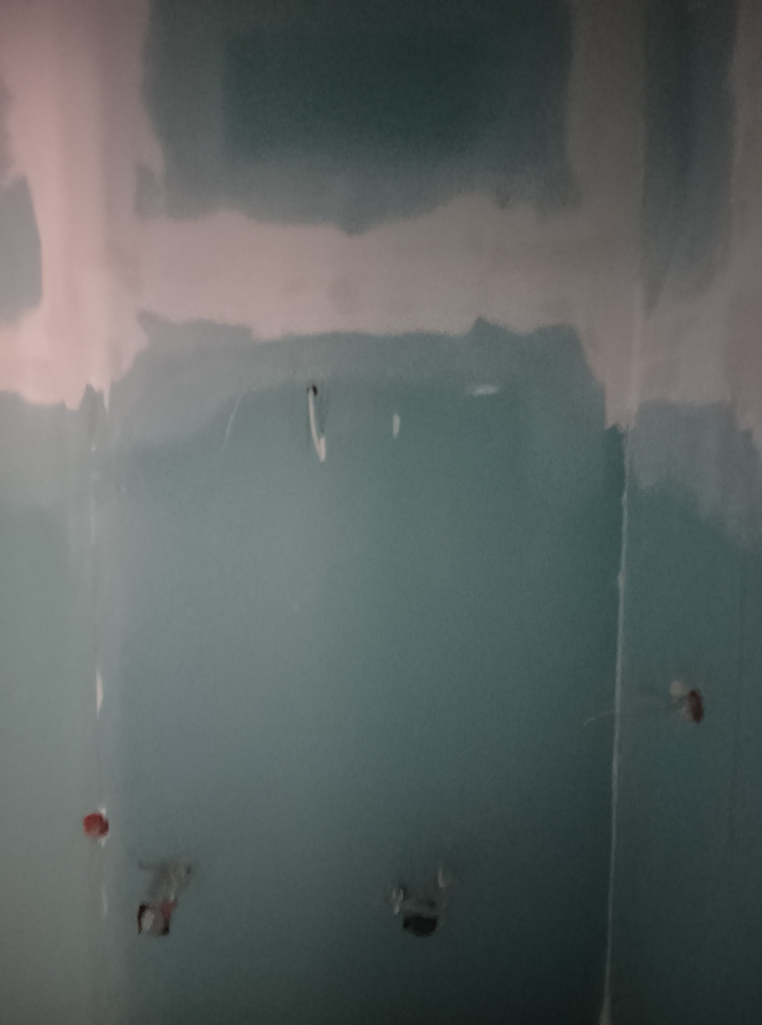 Ściana po nałożeniu pierwszej warstwy gładzi, widoczne otwory na gniazdka elektryczne i niedoskonałości powierzchni. Świeżo nałożona gładź w odcieniach bieli i szarości.