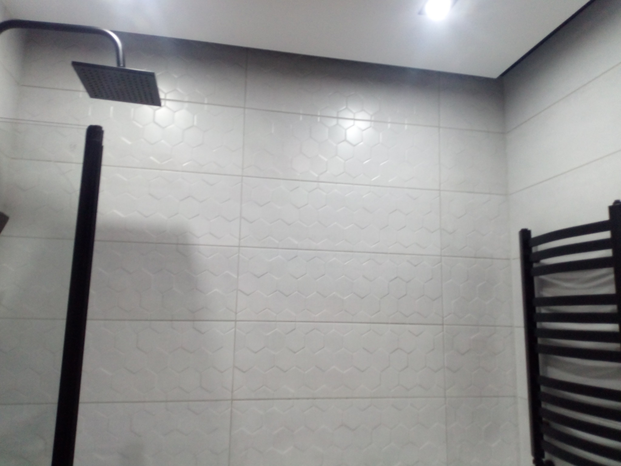 Wykończona łazienka z szarymi, heksagonalnymi płytkami, czarną armaturą i grzejnikiem drabinkowym. Nowoczesny design z minimalistycznym oświetleniem.