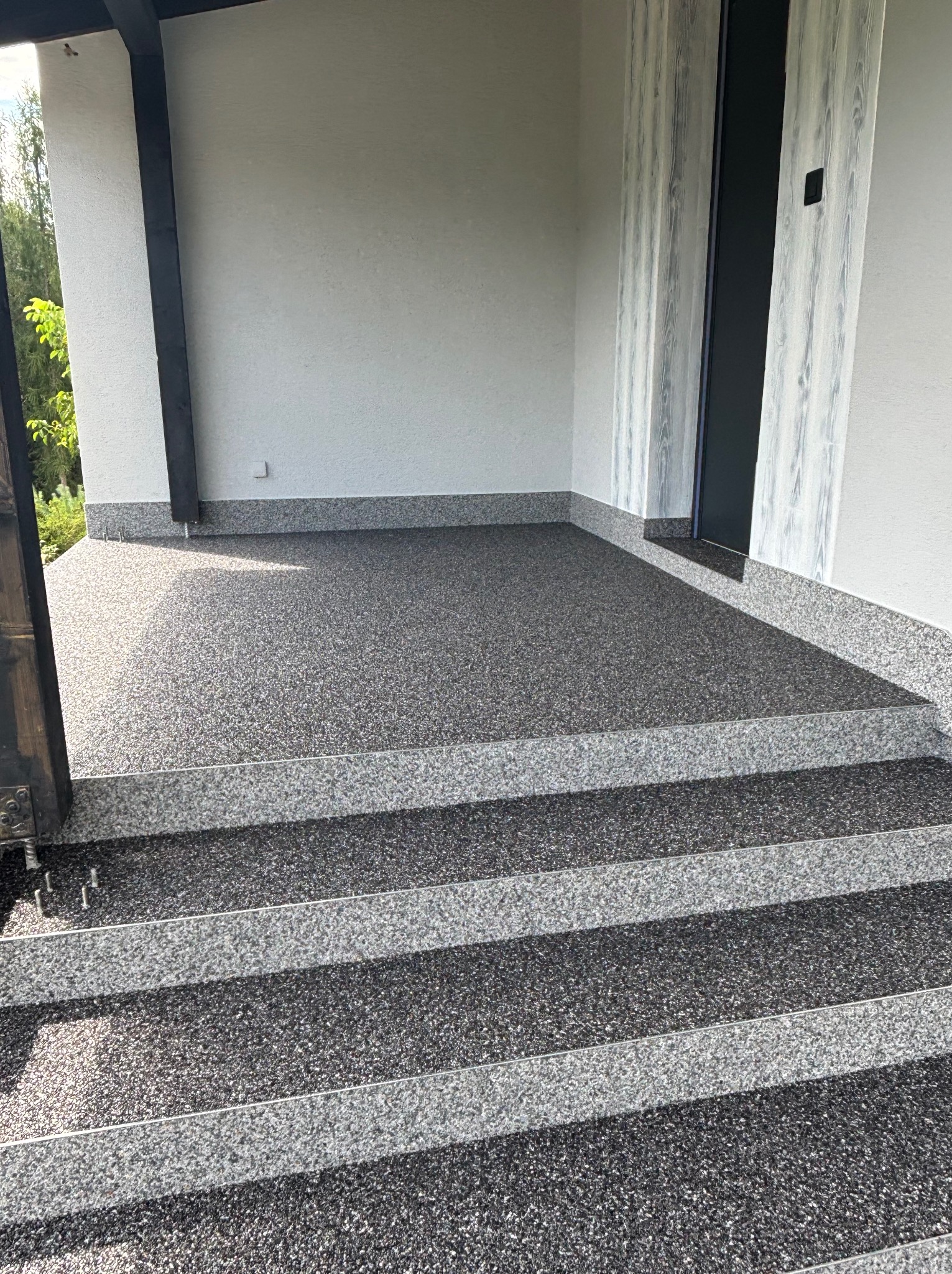 Nowoczesny taras z żywicy epoksydowej w odcieniach szarości, z widocznymi schodami wejściowymi i fragmentem elewacji budynku. Wykończenie z dbałością o detale.