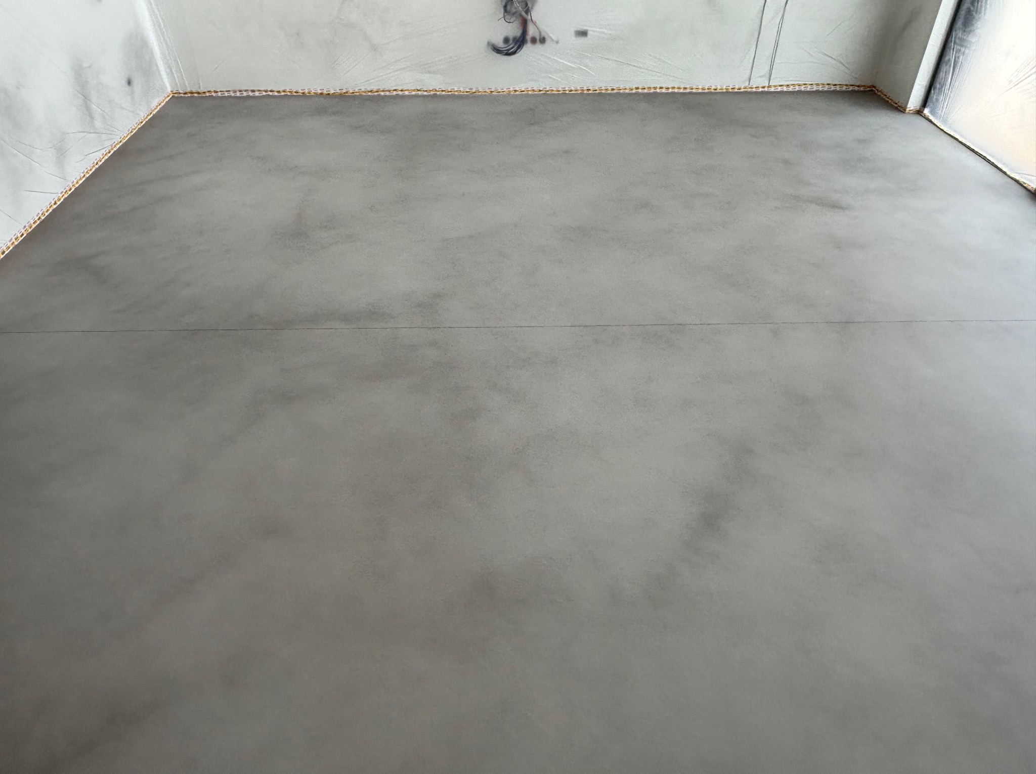 Wnętrze z szarą, gładką posadzką żywiczną, zabezpieczone folią malarską przy ścianach. Widoczne przewody elektryczne na suficie.