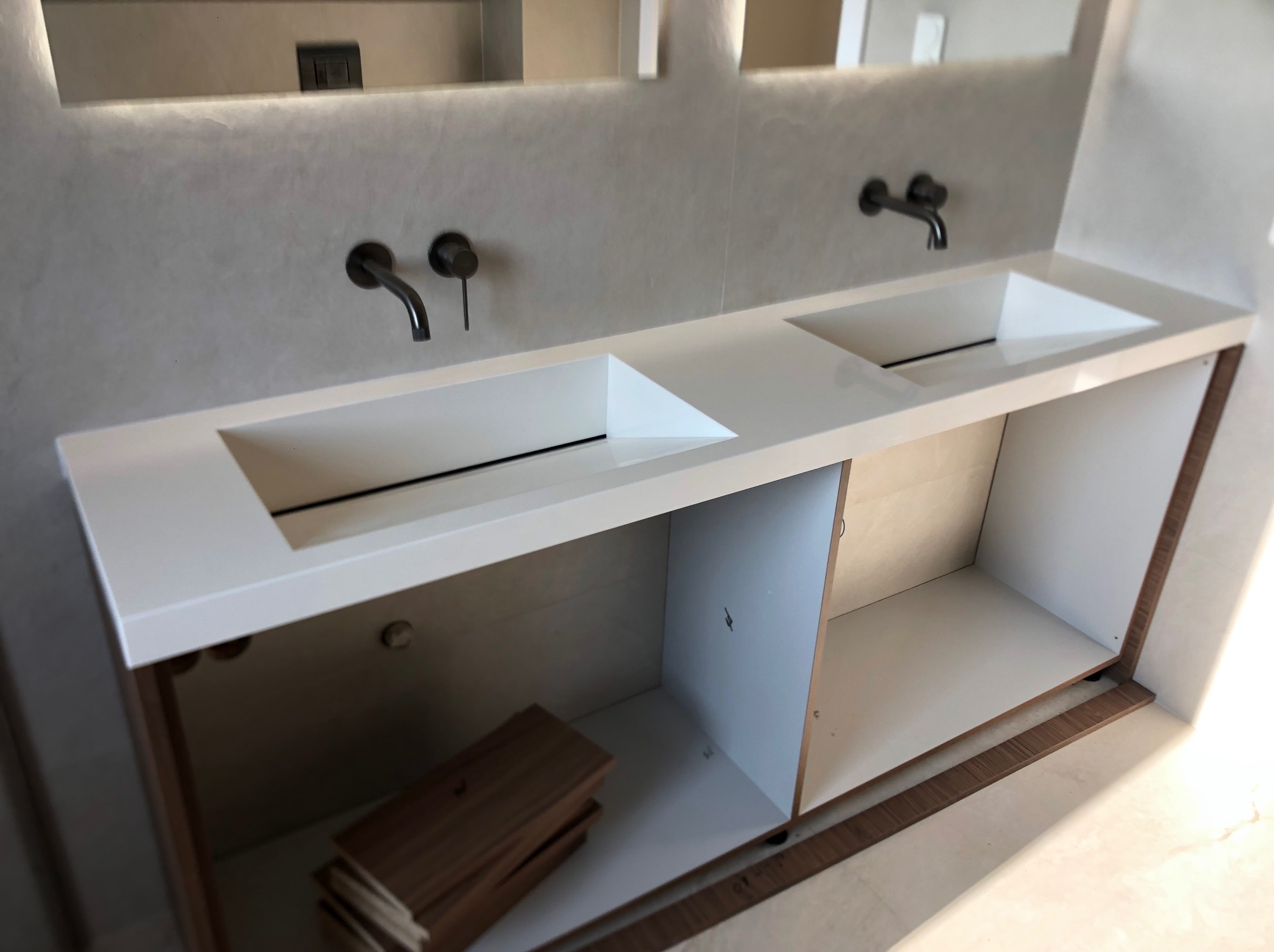 Nowoczesna łazienka z dwoma umywalkami o geometrycznych kształtach, czarną armaturą i szafką z otwartymi półkami. Minimalistyczny design, jasne kolory i subtelne oświetlenie.