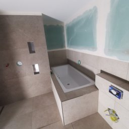 Piotr Bielarczyk - Remont łazienki w trakcie: obudowana wanna, płytki w odcieniach beżu, przygotowane ściany do malowania, widoczne instalacje. Minimalistyczny design.