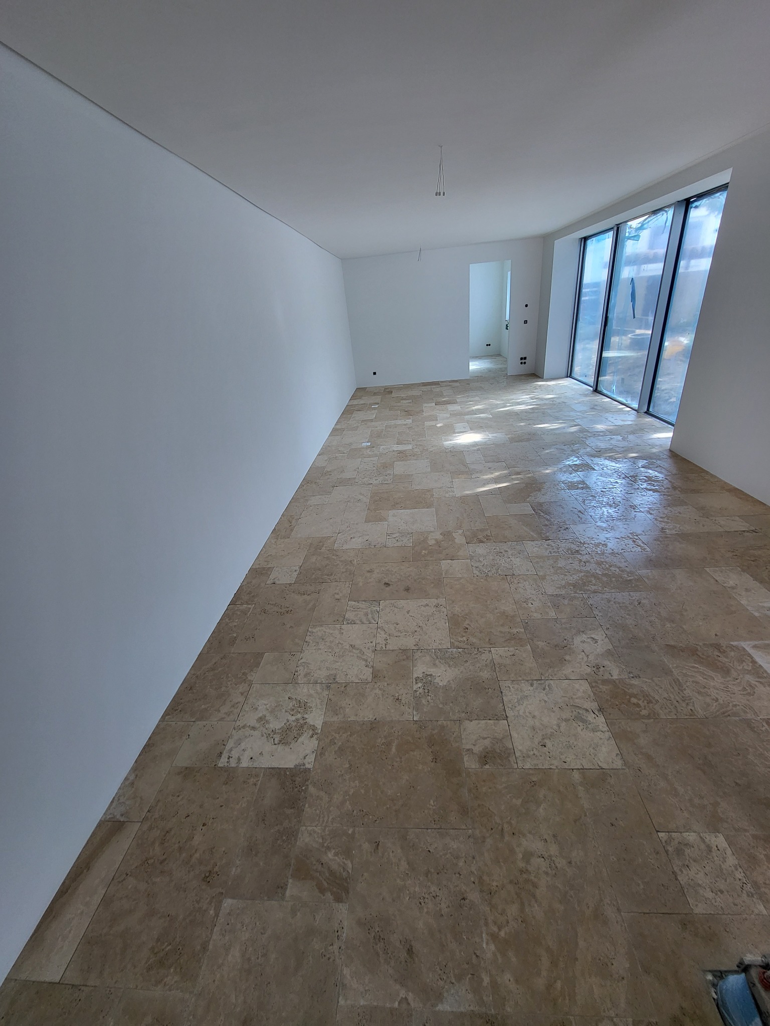 Jasne, przestronne wnętrze z nową, beżową podłogą z płytek. Duże okna z widokiem na zewnątrz. Świeżo pomalowane, białe ściany. Minimalistyczny design.