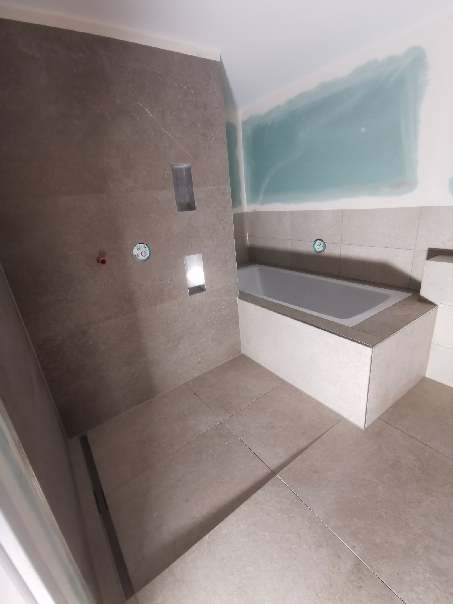 Wykończona łazienka z wanną w zabudowie i wnękami w ścianie wyłożonej płytkami imitującymi kamień. Widoczne przygotowane ściany do malowania.