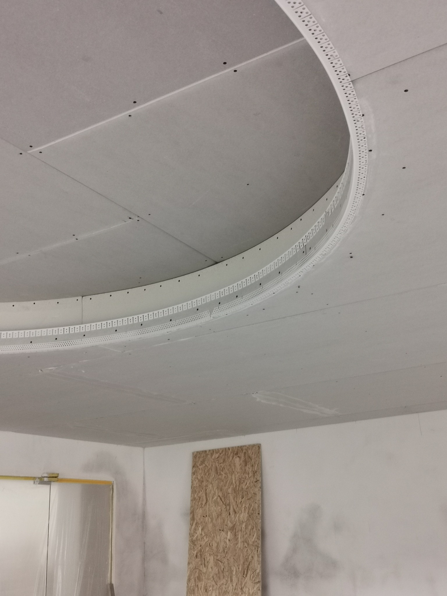 Sufit podwieszany z płyt gipsowo-kartonowych z elementami dekoracyjnymi w kształcie łuku, widoczne ślady szpachlowania na ścianach.