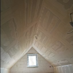 Piotr Dziuba - Poddasze po wstępnym wyrównaniu ścian i sufitu, widoczne łączenia płyt i niedoskonałości przed finalnym wykończeniem. Okno w szczycie doświetla wnętrze.