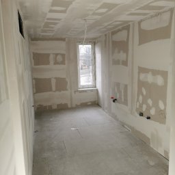 Piotr Dziuba - Wnętrze w trakcie prac wykończeniowych w Jastrowie. Widoczne ściany z nałożonymi warstwami wyrównującymi, przygotowane do dalszych prac malarskich.