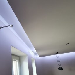 Piotr Dziuba - Wykończony sufit podwieszany z oświetleniem LED i karniszami, widok z dołu. Minimalistyczny design, gładkie powierzchnie, nowoczesne lampy wiszące.
