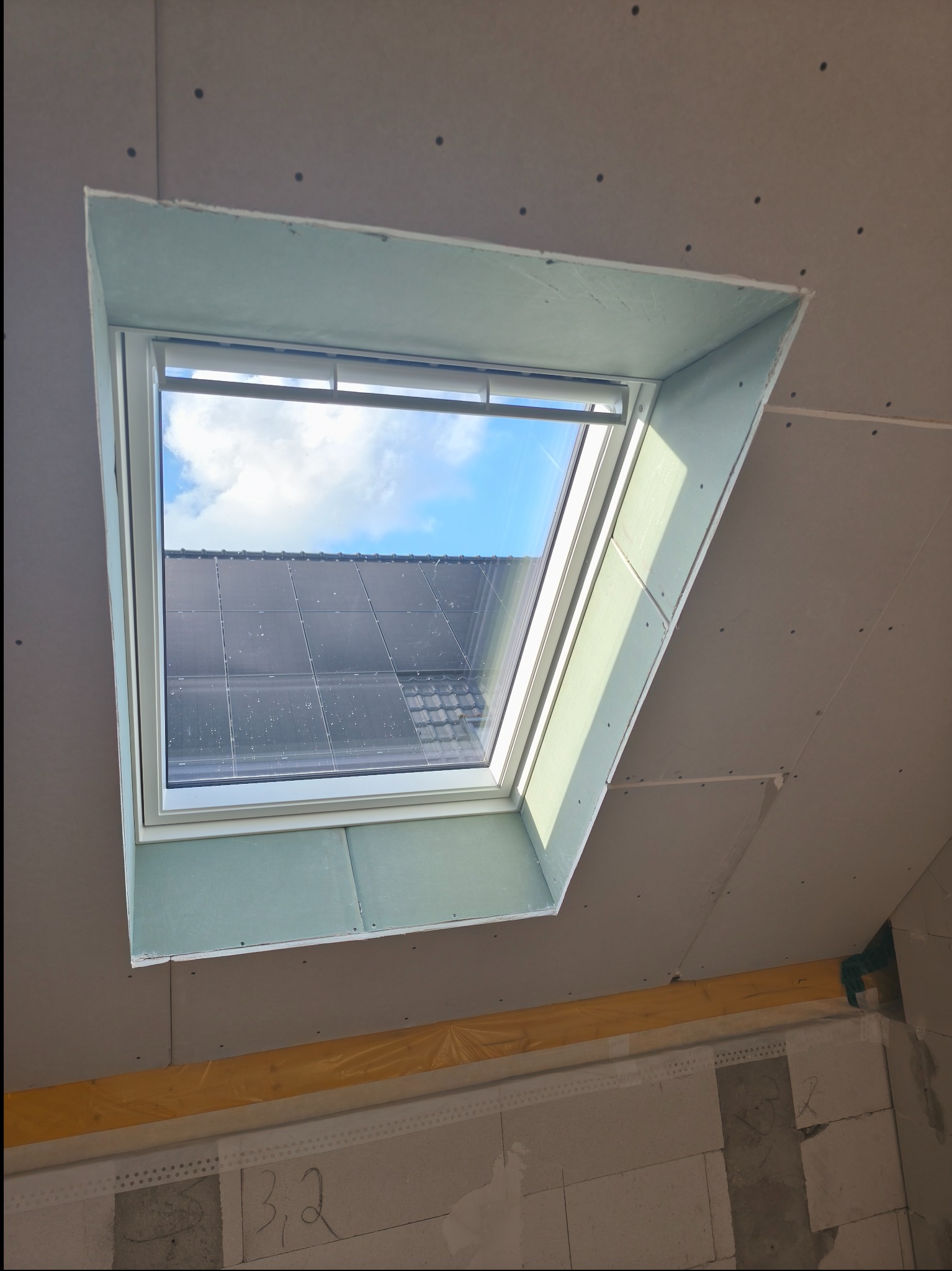 Montaż płyty karton gips wokół okna dachowego, widoczne łączenia płyt i konstrukcja nośna. Etap prac wykończeniowych w pomieszczeniu.