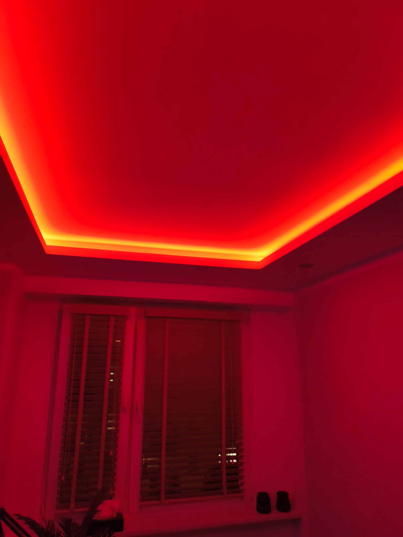 Czerwone oświetlenie LED na suficie podwieszanym, widok na okno z żaluzjami. Nowoczesny design wnętrza z intensywnym, nastrojowym światłem.
