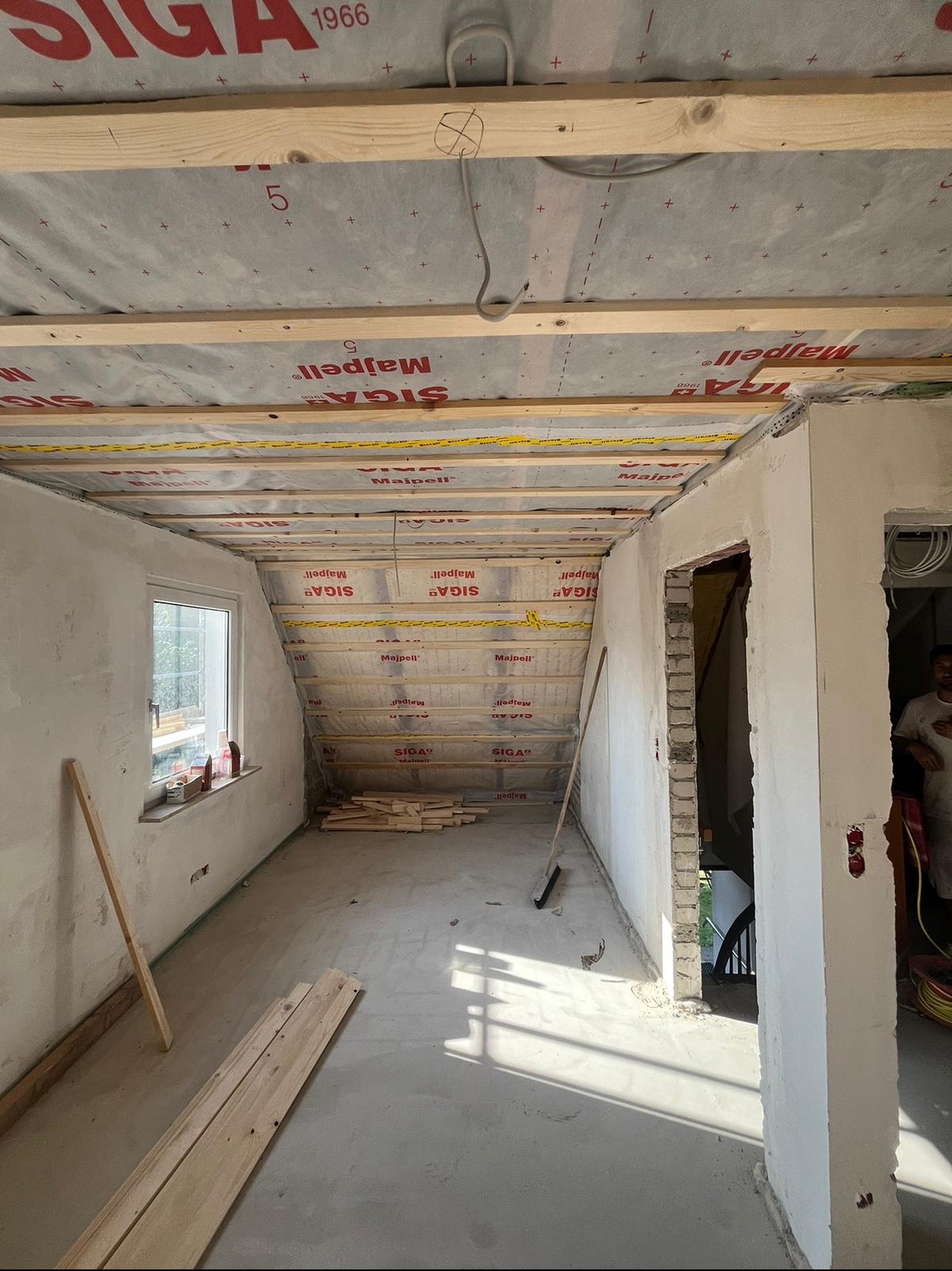 Poddasze w trakcie prac wykończeniowych: drewniana konstrukcja dachu z izolacją, surowe ściany, przygotowane deski na podłodze, widoczne instalacje elektryczne.