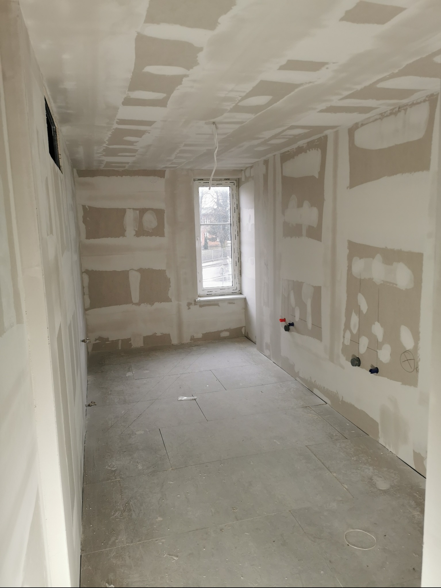 Wnętrze w trakcie prac wykończeniowych w Jastrowie. Widoczne ściany z nałożonymi warstwami wyrównującymi, przygotowane do dalszych prac malarskich.