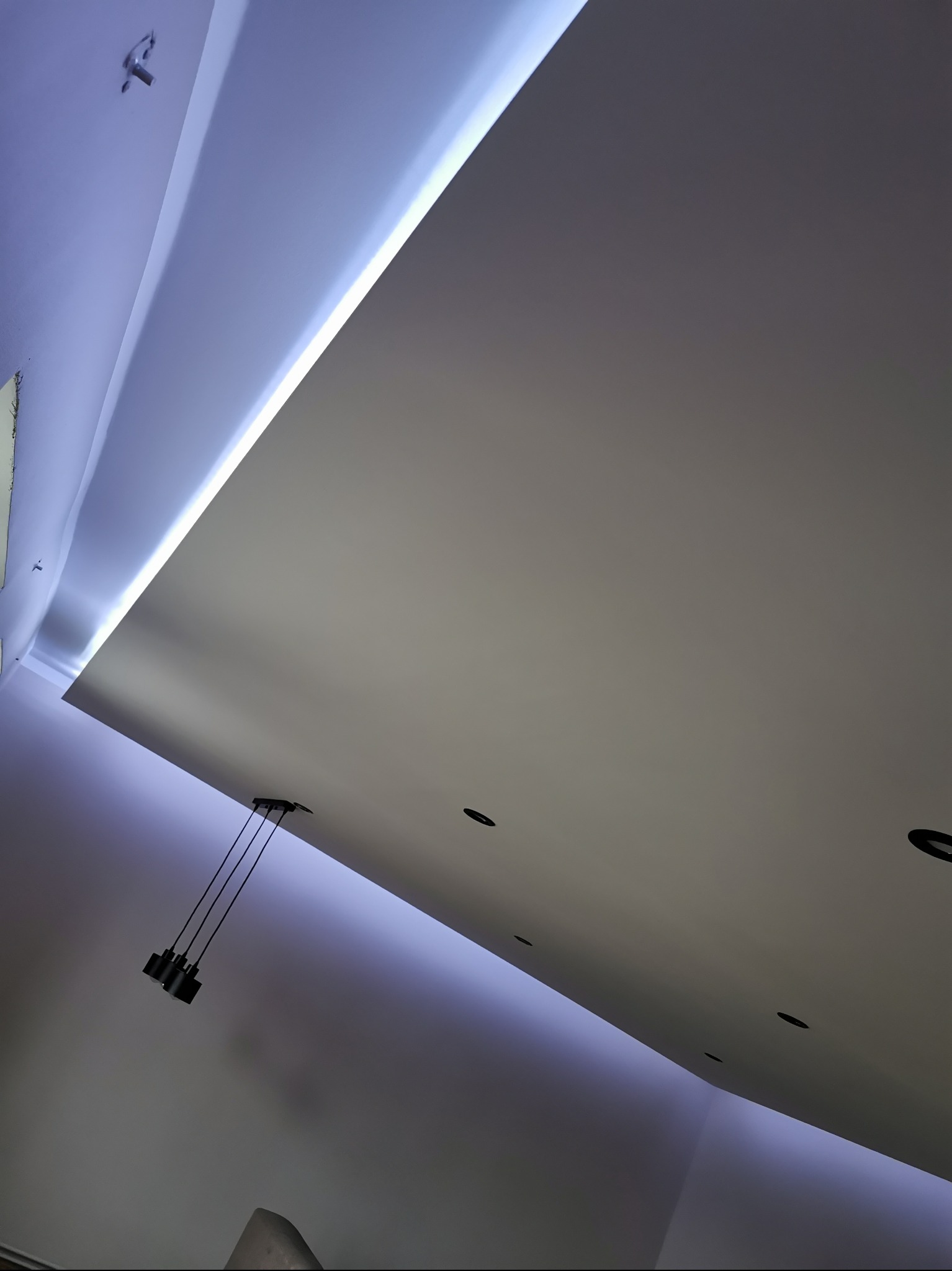 Nowoczesny sufit podwieszany z oświetleniem LED i punktowymi lampami, widziany pod kątem. Minimalistyczny design, gładka powierzchnia, subtelne światło.