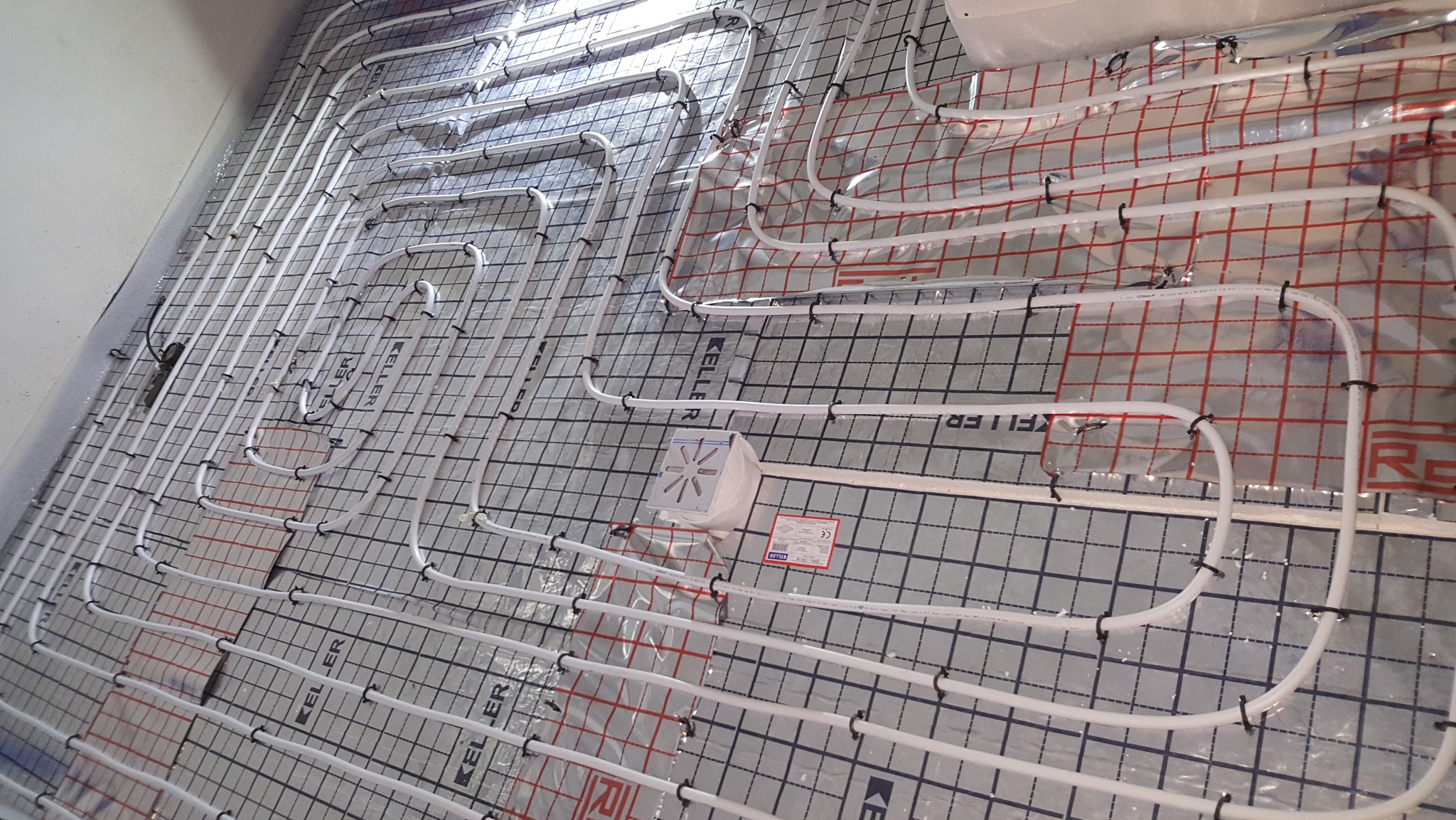 Białe rury ogrzewania podłogowego ułożone na izolacji w Piasecznie, widok z góry. Równomierny rozkład rur na powierzchni, gotowe do zalania wylewką.