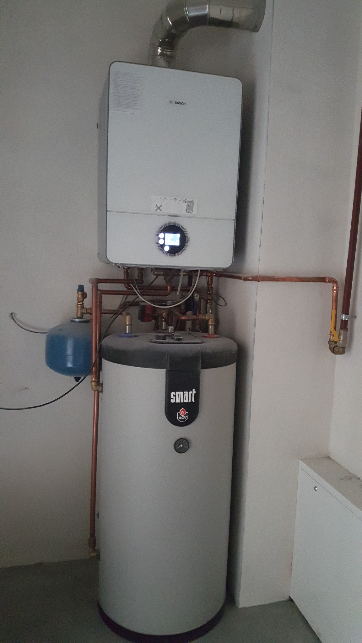 Zmontowany piec gazowy Bosch z zasobnikiem ACV Smart w Piasecznie. Widoczne miedziane rury instalacji i niebieski zbiornik wyrównawczy. Nowoczesny system grzewczy.