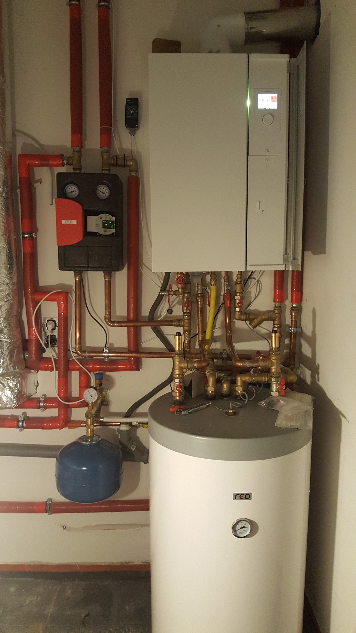 Zmontowany, nowoczesny piec gazowy z zasobnikiem ciepłej wody i rozbudowaną instalacją hydrauliczną z rur miedzianych i zaworów, umieszczony w pomieszczeniu technicznym.