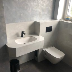 KarolH. - Nowoczesna łazienka po remoncie: szare ściany z efektem betonu, podwieszana toaleta i umywalka z czarną armaturą. Minimalistyczny design, widok na okno.
