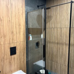 KarolH. - Nowoczesna łazienka z kabiną prysznicową typu walk-in, drewnianymi panelami ściennymi i wiszącą toaletą. Minimalistyczny design z akcentami drewna i szarości.