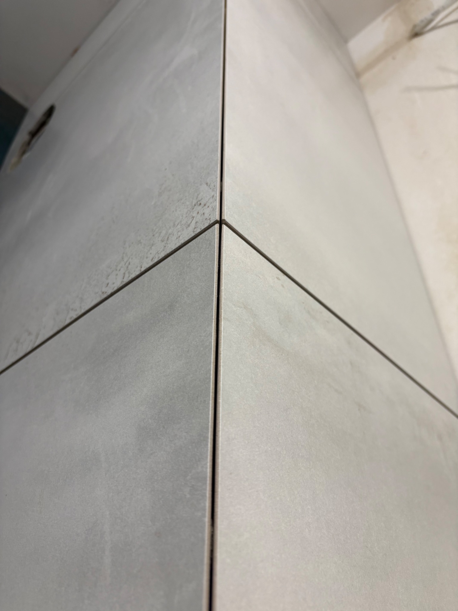 Szczegółowe ujęcie narożnika wykończonego szarymi, matowymi płytkami wielkoformatowymi z wąską fugą. Widoczne delikatne cieniowanie i struktura płytek.