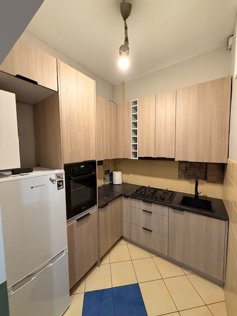 Jasna kuchnia na wymiar z drewnopodobnymi frontami, czarnym blatem i sprzętami AGD. Uwagę zwraca wnęka na wino i nietypowe oświetlenie sufitowe.