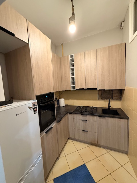 Jasna kuchnia na wymiar z drewnianymi frontami, czarnym blatem i sprzętem AGD. Widoczny fragment ściany z instalacją. Ujęcie z perspektywy podłogi.