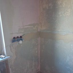 Jonatan Wiśniewski JON-BUD - Przygotowanie ściany do malowania: gładź na siatce, widoczne gniazdka elektryczne zabezpieczone folią, surowy stan przed wykończeniem.