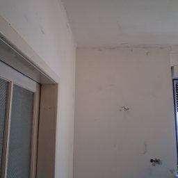 Jonatan Wiśniewski JON-BUD - Przygotowanie ścian do malowania w Łodzi: ściana po szpachlowaniu, widoczne ślady po gładzi, gotowa do nałożenia farby. Fragment okna i drzwi.