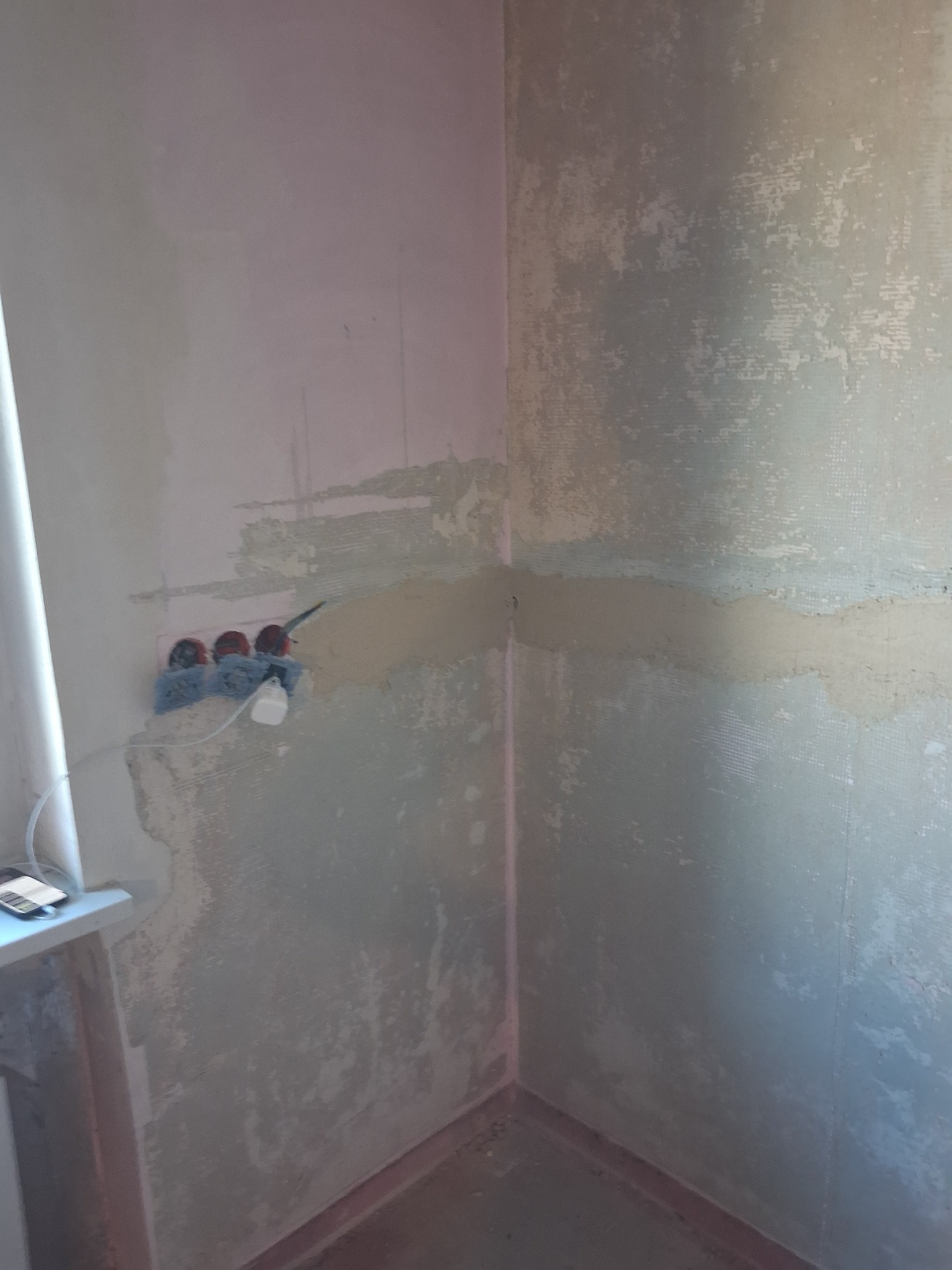 Przygotowanie ściany do malowania: gładź na siatce, widoczne gniazdka elektryczne zabezpieczone folią, surowy stan przed wykończeniem.