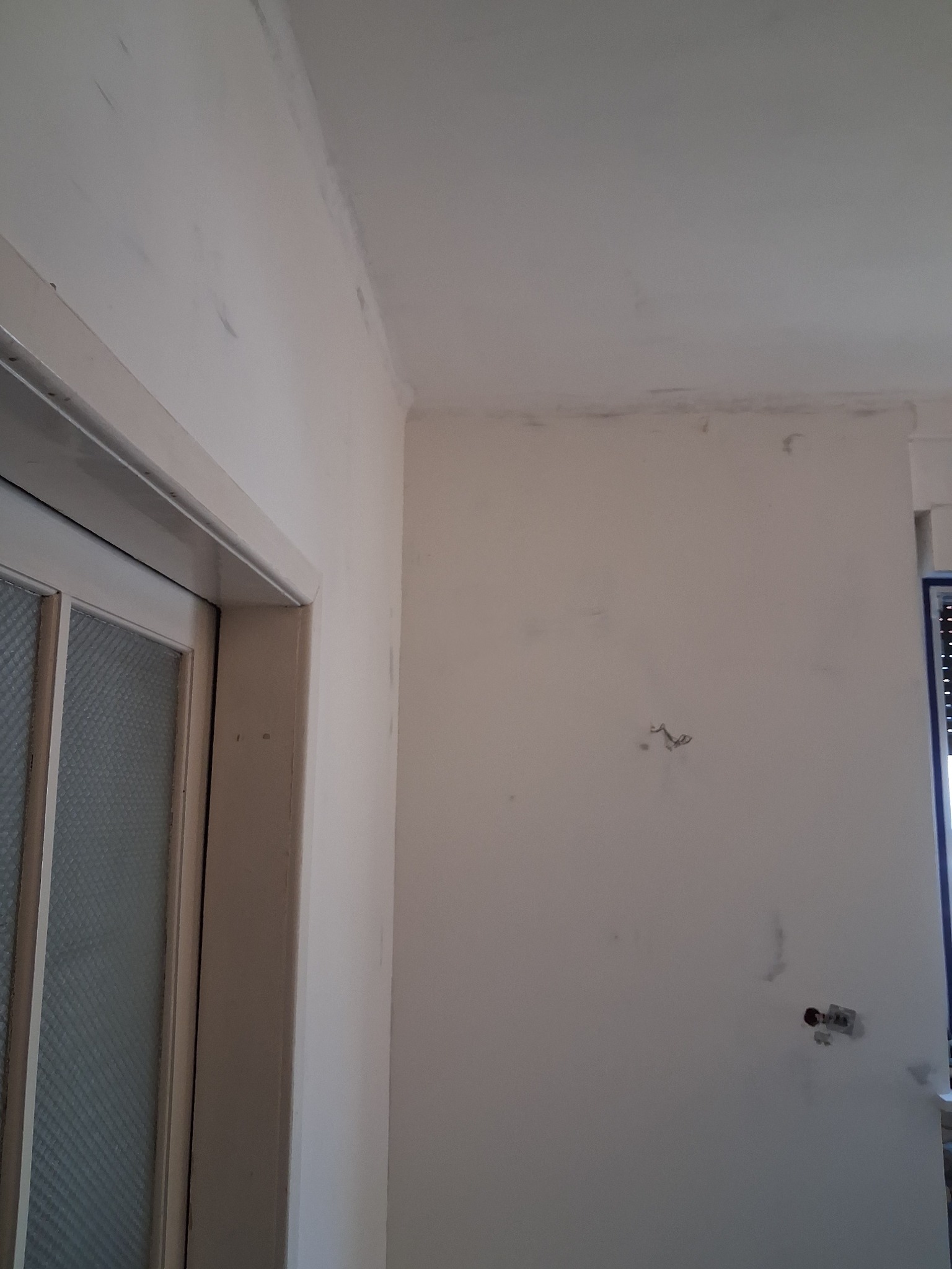 Przygotowanie ścian do malowania w Łodzi: ściana po szpachlowaniu, widoczne ślady po gładzi, gotowa do nałożenia farby. Fragment okna i drzwi.