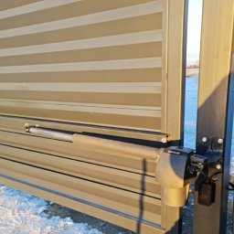 Electric House Tomasz Galoch - Automatyka do bramy przesuwnej z widocznym siłownikiem marki Genius, częściowo otwarta, w tle ośnieżone pole i błękitne niebo.