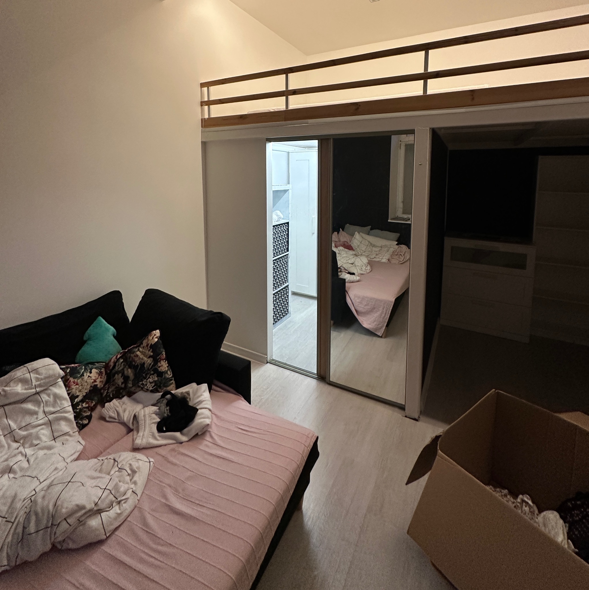 Pokój z antresolą i rozsuwanymi drzwiami szafy wnękowej, w której widać wnętrze innego pokoju. Wnętrze w trakcie remontu lub przeprowadzki, widoczne kartony.