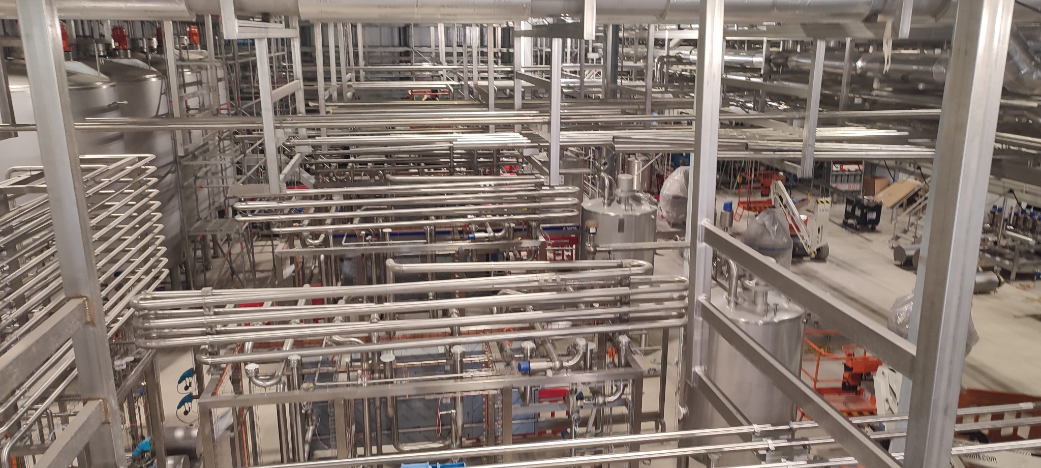 Kompleksowa instalacja przemysłowa z rurami ze stali nierdzewnej, zbiornikami i konstrukcjami wsporczymi. Widok z góry ukazuje skomplikowany układ rurociągów.