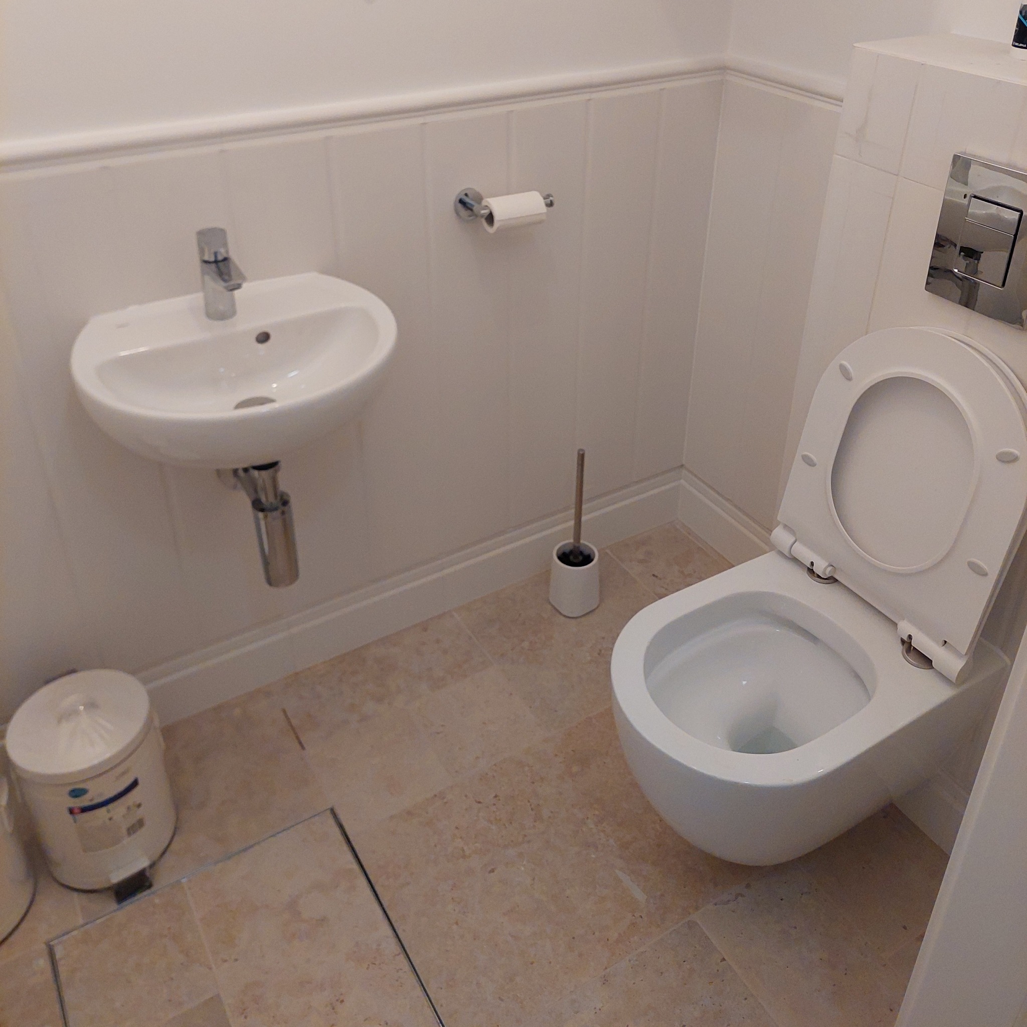 Biała toaleta i umywalka w małej łazience po remoncie w Grójcu. Beżowe płytki podłogowe i białe panele ścienne. Minimalistyczny design.