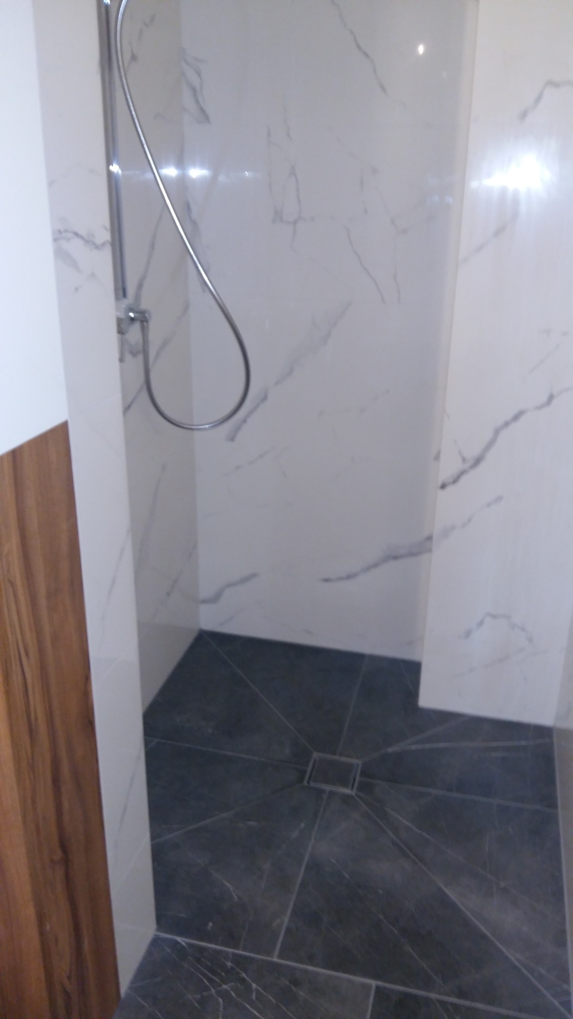 Nowoczesna kabina prysznicowa z marmurowymi płytkami ściennymi i ciemną, geometryczną posadzką. Widoczny chromowany zestaw prysznicowy.