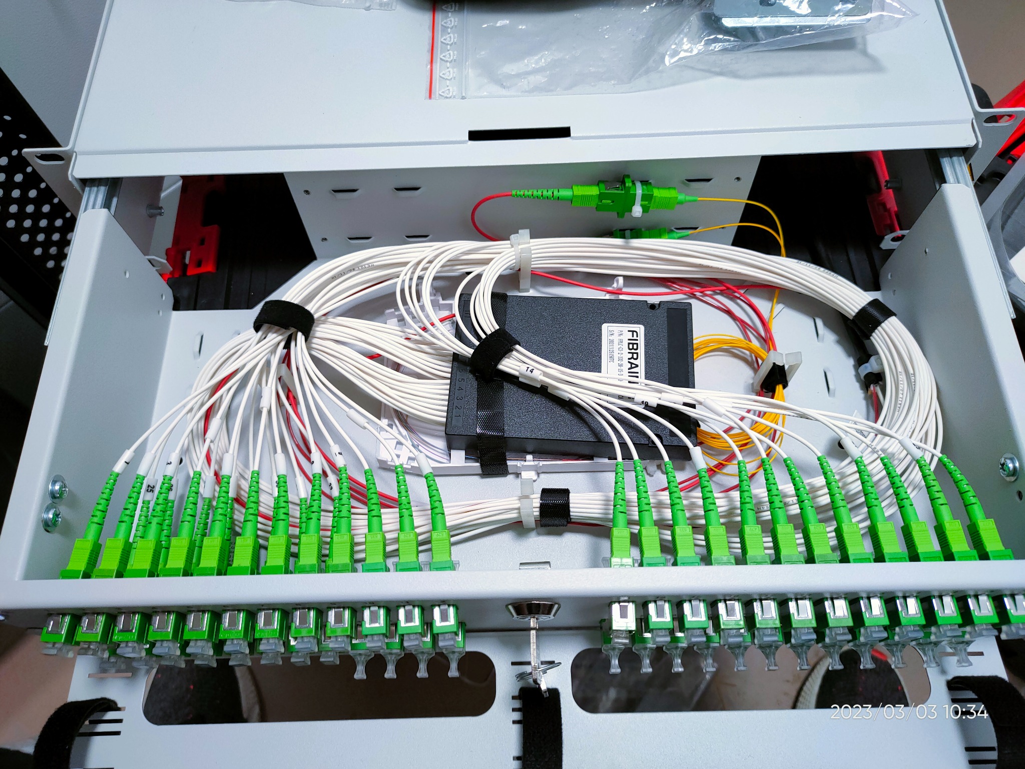 Rozdzielnica światłowodowa z podłączonymi kablami zakończonymi zielonymi złączami. Uporządkowane przewody wewnątrz szafy telekomunikacyjnej. Widoczne oznaczenia na kablach.