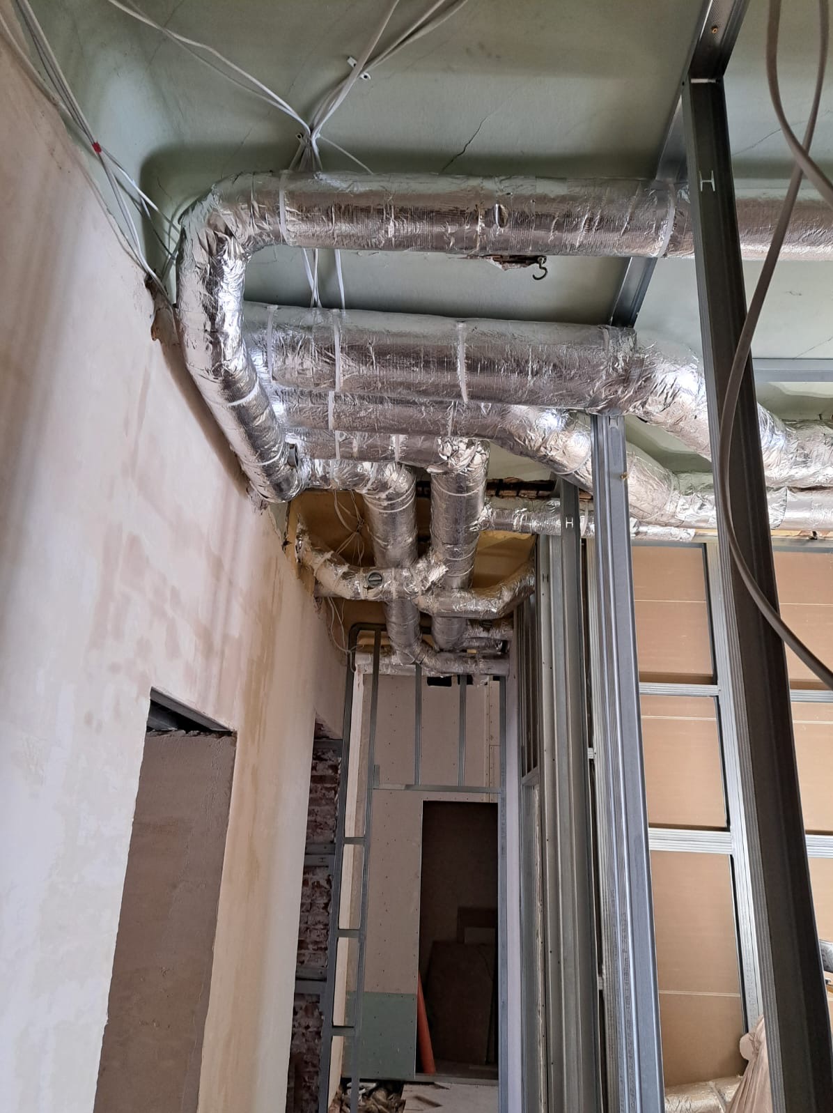 Montaż izolowanych przewodów wentylacyjnych pod sufitem w budynku w trakcie remontu. Widoczne metalowe profile konstrukcyjne i instalacje.