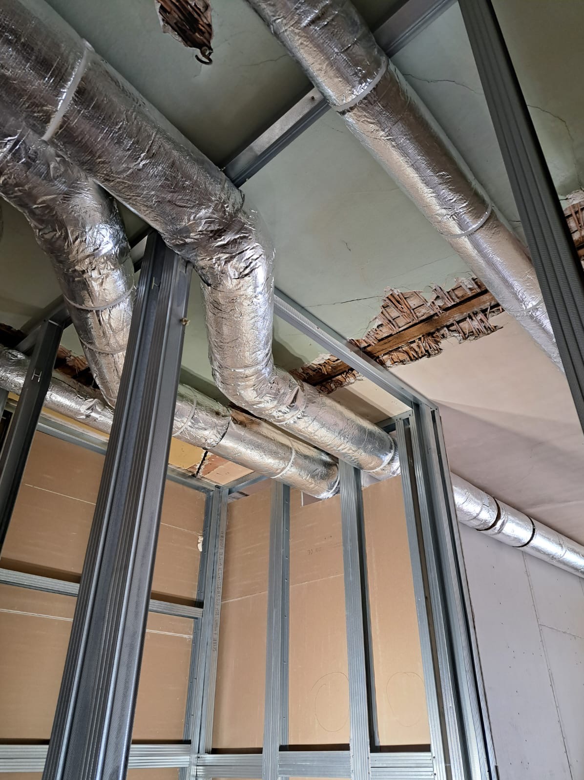 Montaż izolowanych przewodów wentylacyjnych pod sufitem podwieszanym z metalową konstrukcją. Widoczne uszkodzenia starego sufitu.