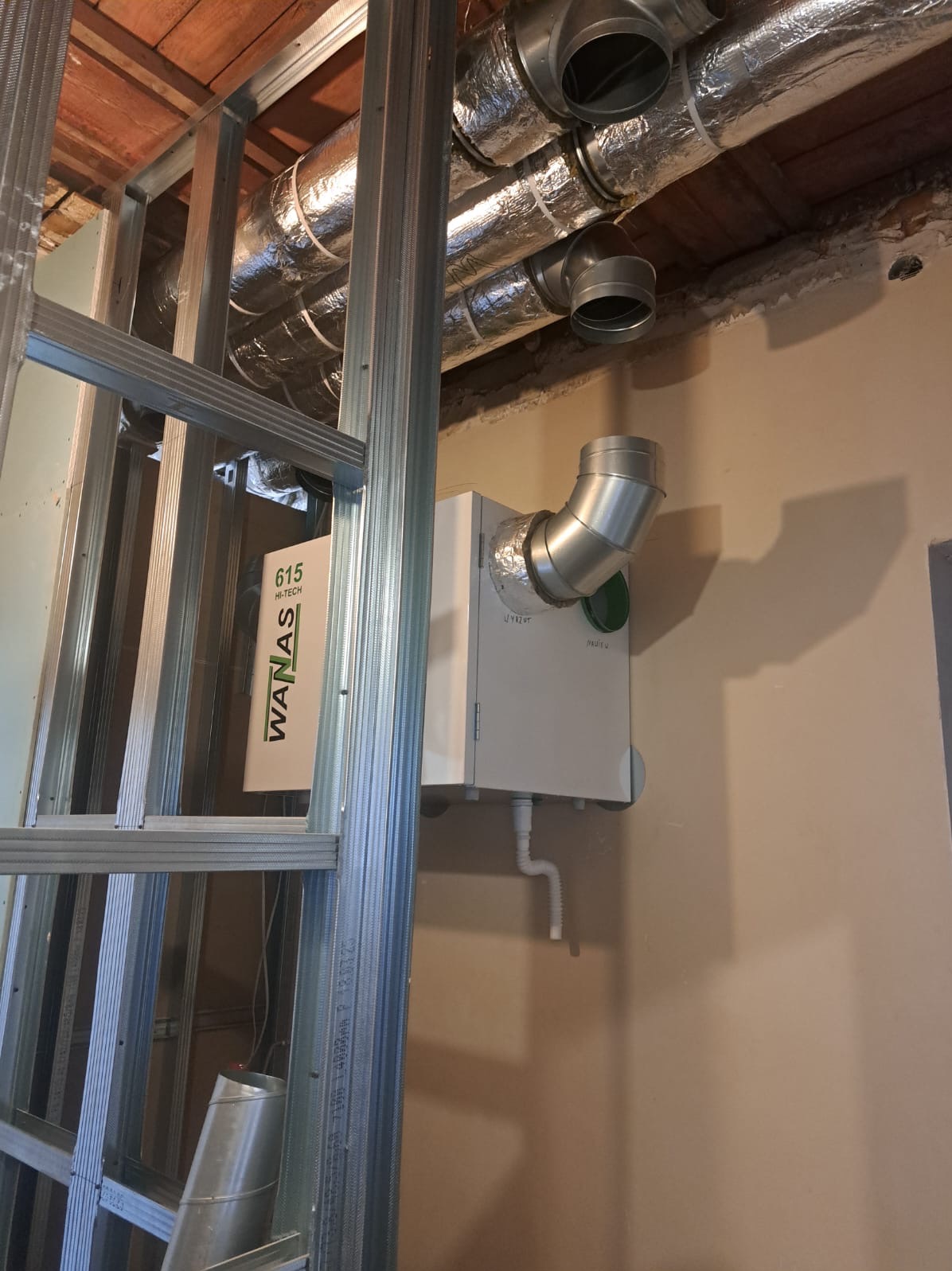 Montaż rekuperacji: centrala wentylacyjna WANAS 615 Hi-Tech z podłączonymi przewodami wentylacyjnymi, widoczne elementy konstrukcji metalowej.