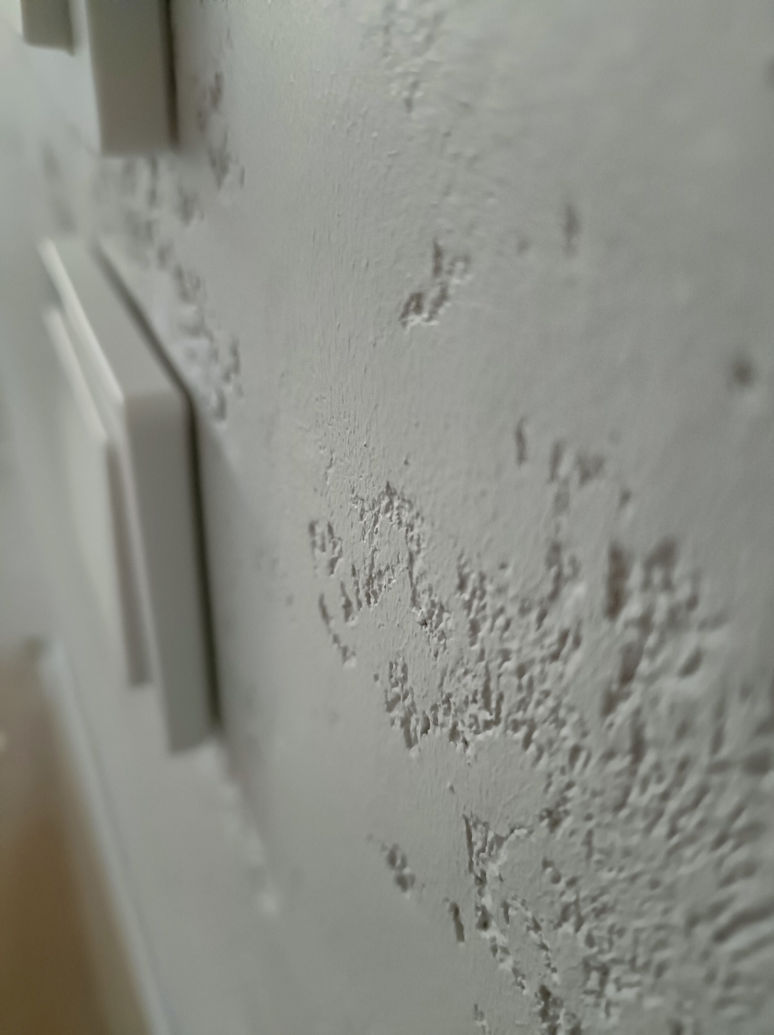 Biała ściana z fakturą w zbliżeniu, widoczne włączniki światła. Wykończenie wnętrz w Warszawie z dbałością o detale.